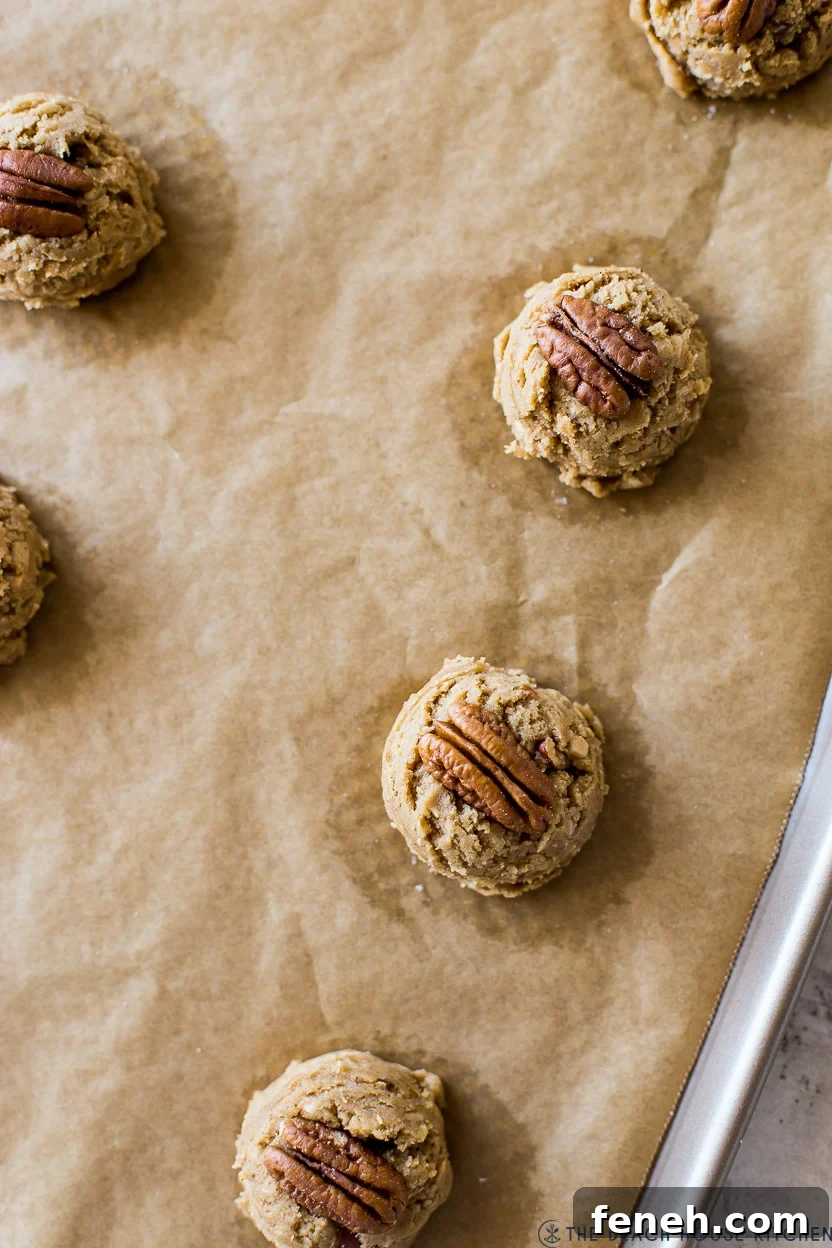 Overhead photo of a baking sheet topped with cookie dough balls topped with pecan halves