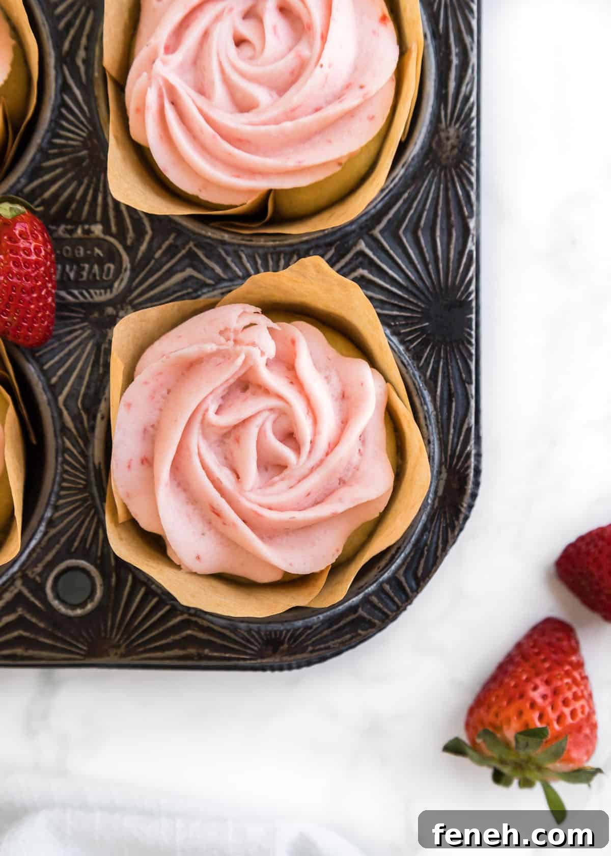 Close up shot of baked strawberry buttercream cupcake with full strawberries accenting the edges of the photo.