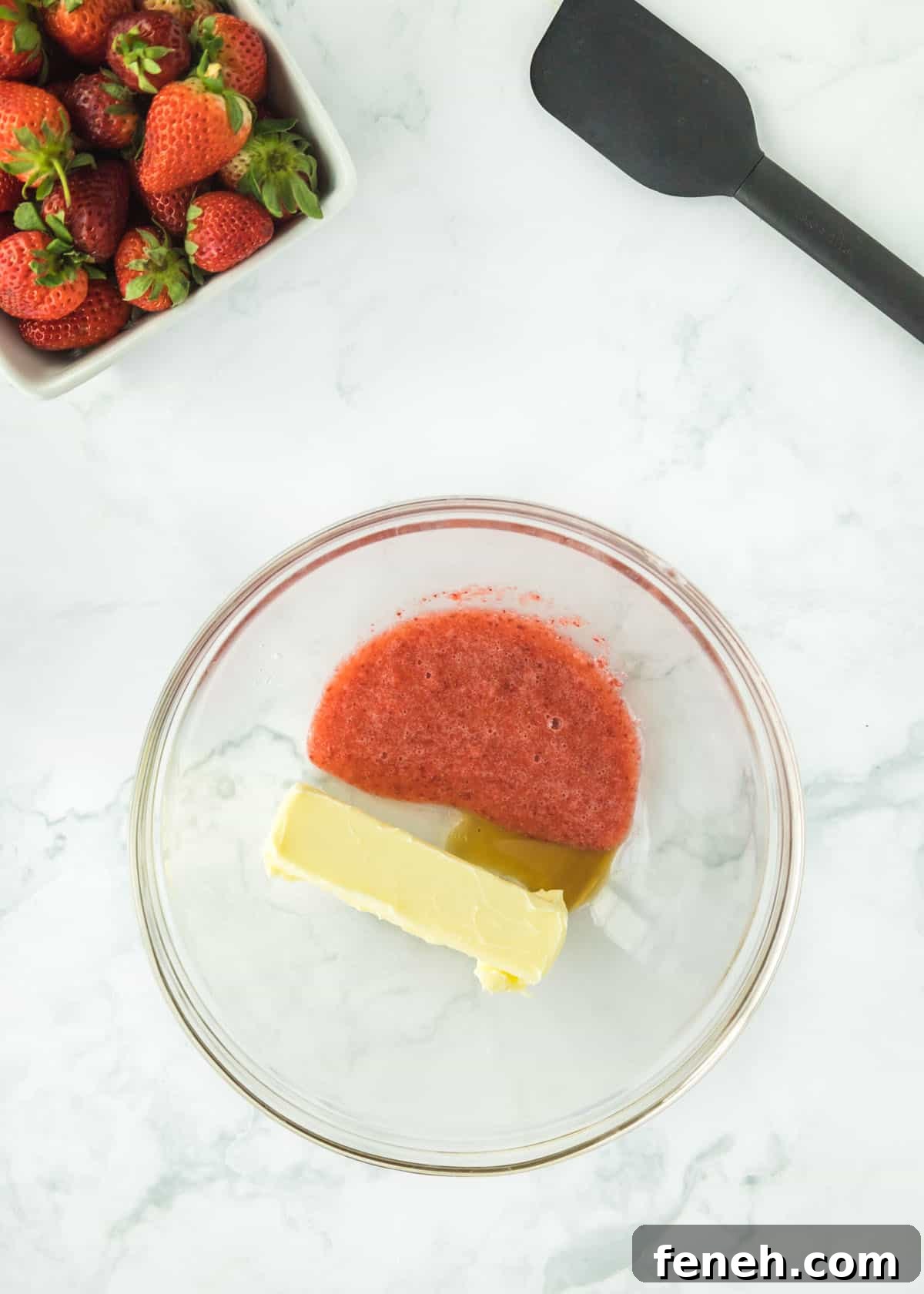 Overhead photo of pureed strawberries with one full stick of butter and vanilla. The upper left and right corners are accented with whole strawberries and a black spatula.