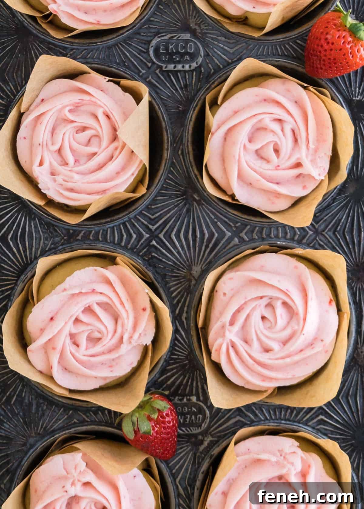 Overhead shot of fully baked strawberry buttercream cupcakes in a cupcake tin with full strawberries accenting the edges of the tin.