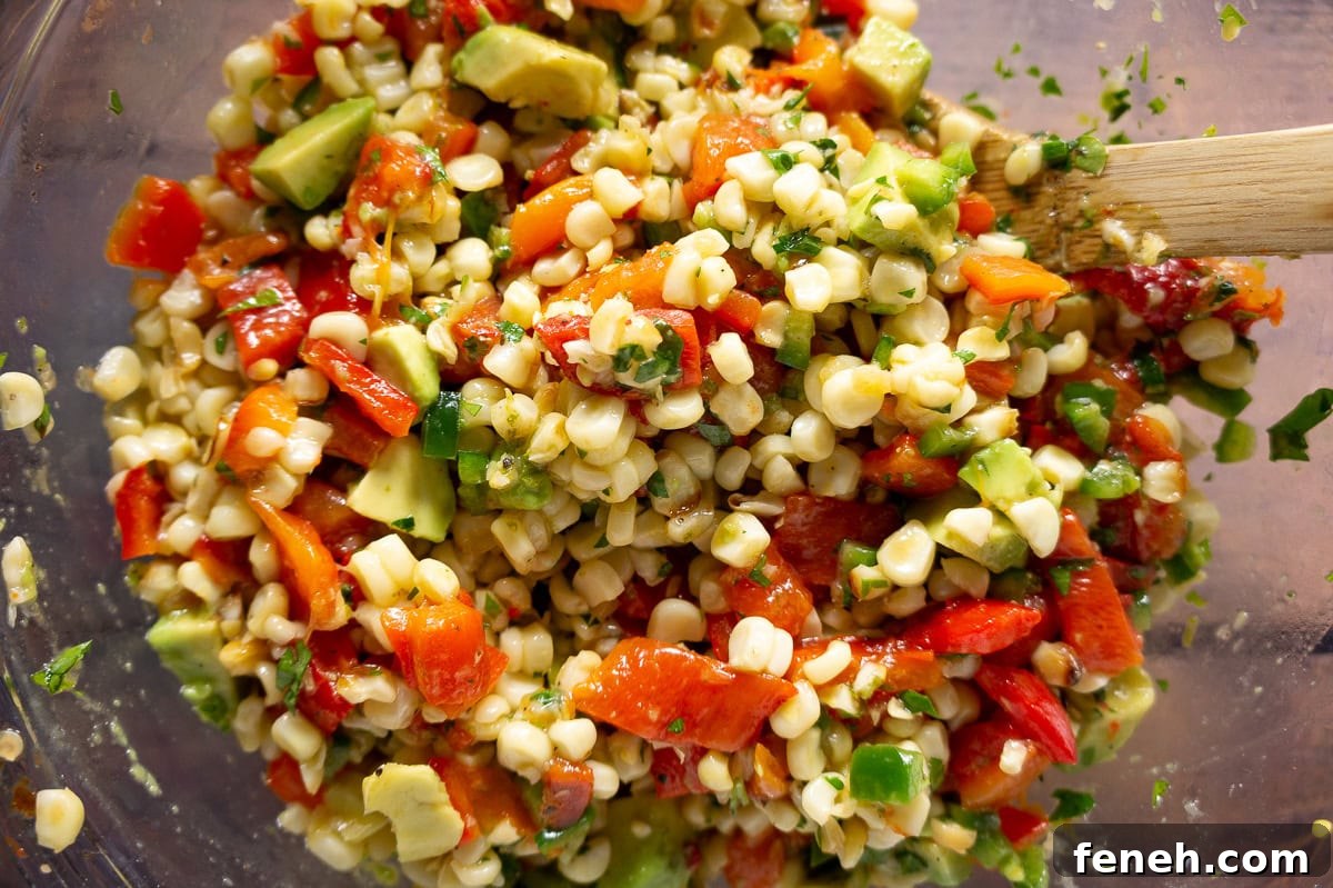 a bowl of mixed corn avocado salad with red peppers and herbs.