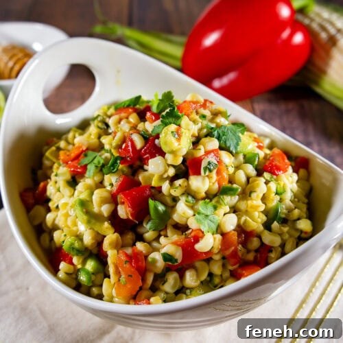 A bowl of corn salad with avocado, red pepper, and herbs.