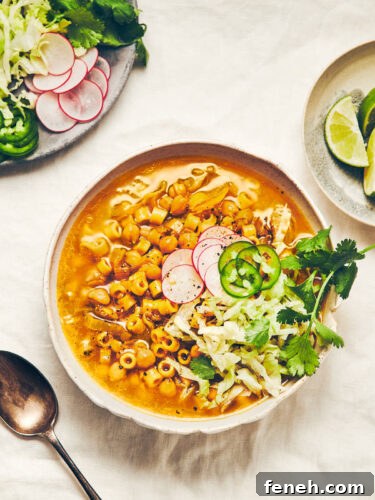 A bowl of chickpea (garbanzo bean) noodle soup topped with shredded lettuce, jalapenos and radish, sitting on a white linen tablecloth
