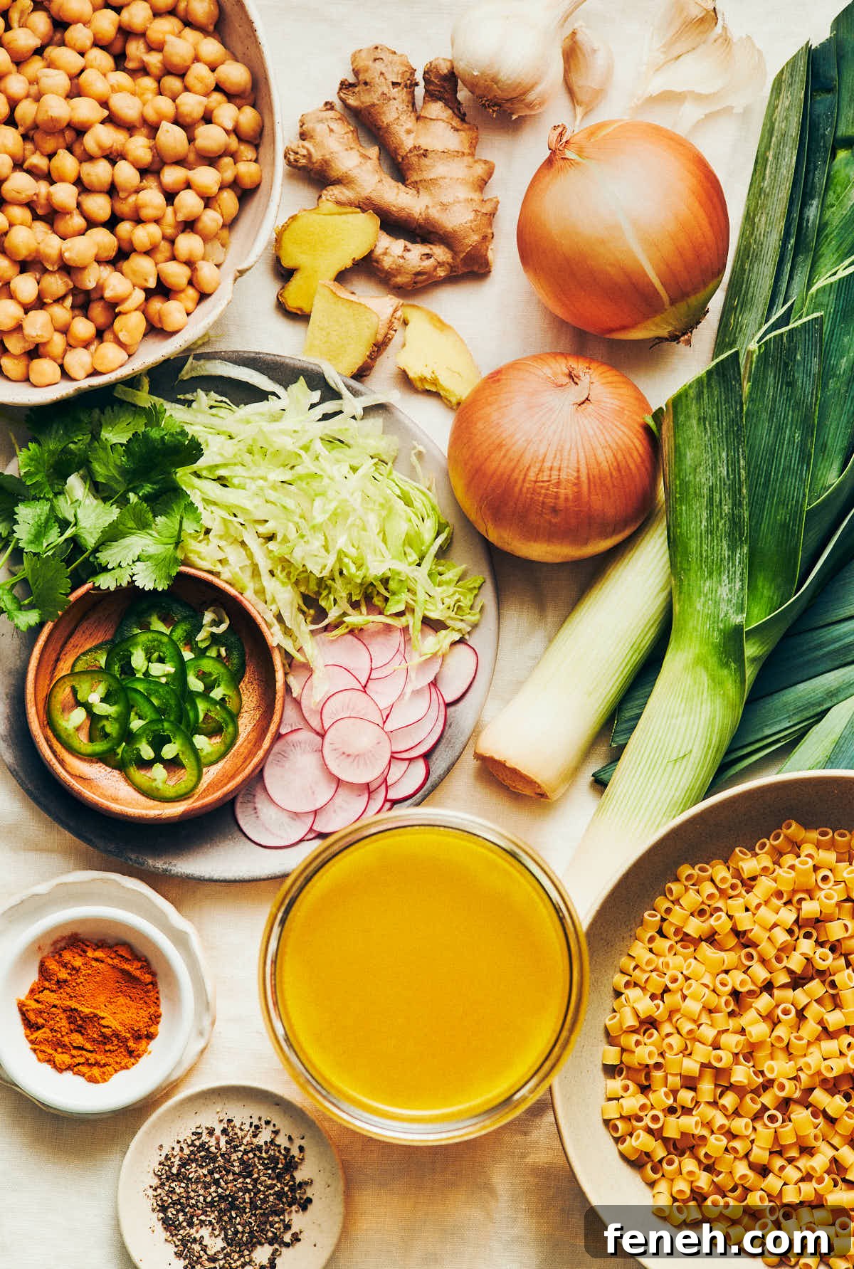 The ingredients to make vegan golden chickpea noodle soup: leeks, yellow onions, vegetable broth, chickpeas, pasta, ginger, turmeric, and black pepper