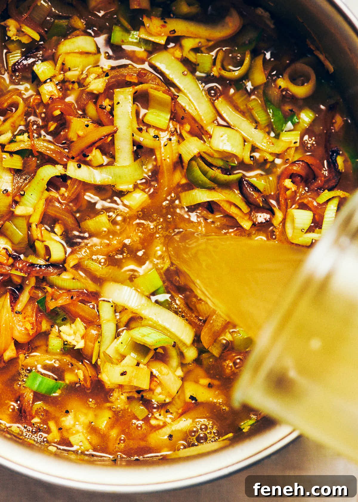 Vegetable stock being poured out of a glass jar, into a large pot of soup