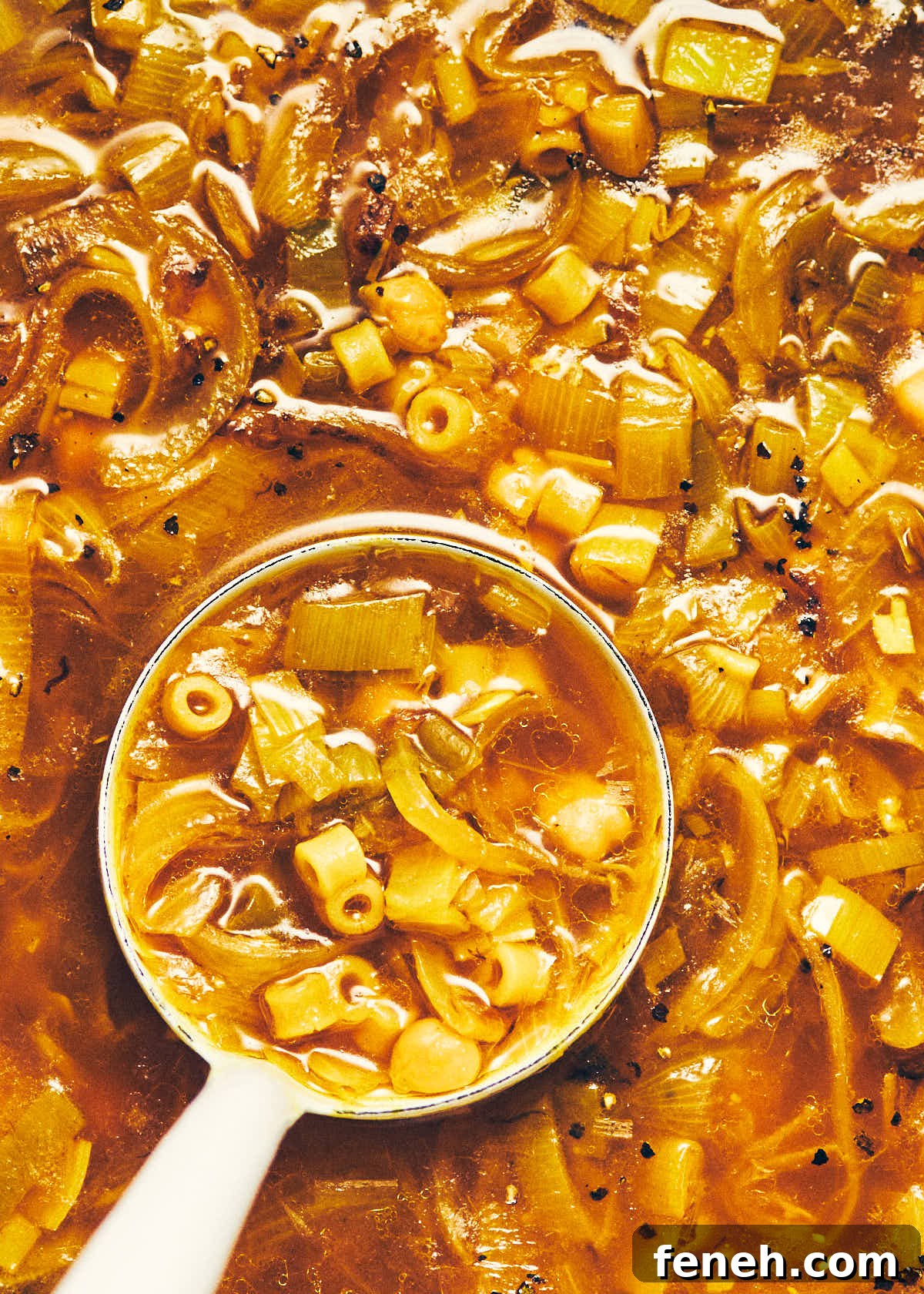 A ladle scooping out vegan golden chickpea noodle soup from a pot