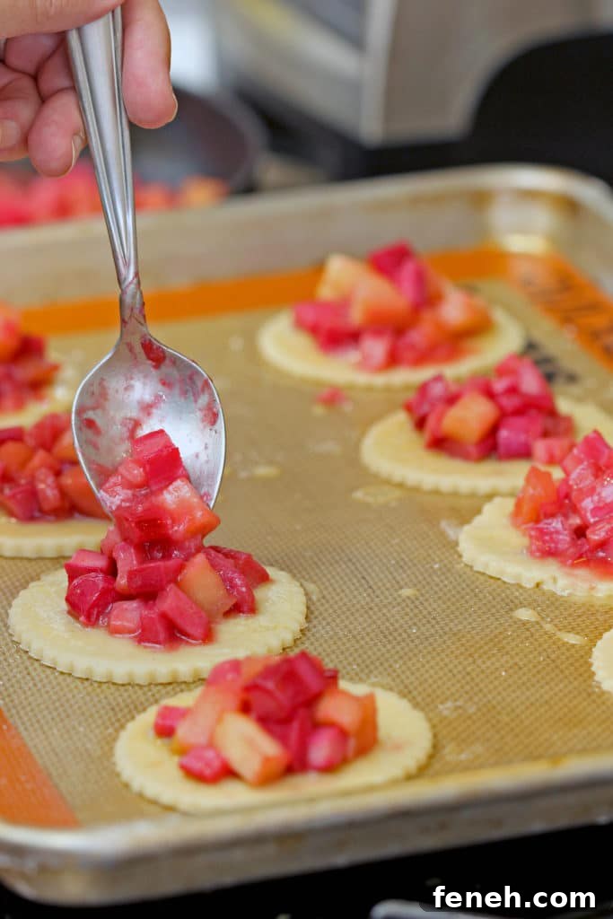closeup side view: filling being added to dough circles on sheet pan