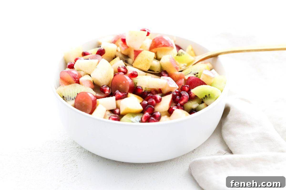 Fall fruit salad in a white serving bowl with a gold serving spoon.