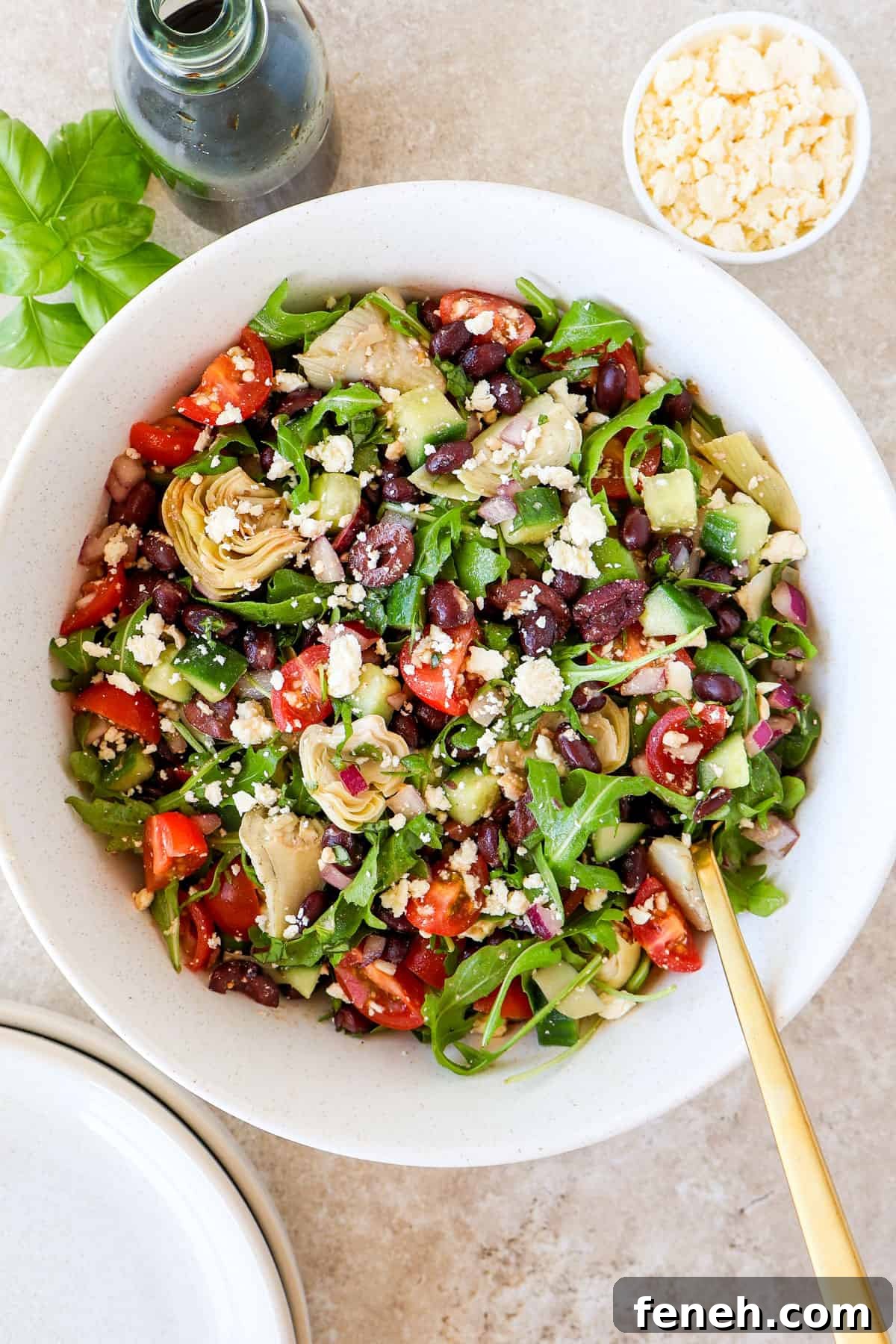 Black bean salad in a bowl with a gold spoon. Balsamic jug, basil, feta and bowls on the side.