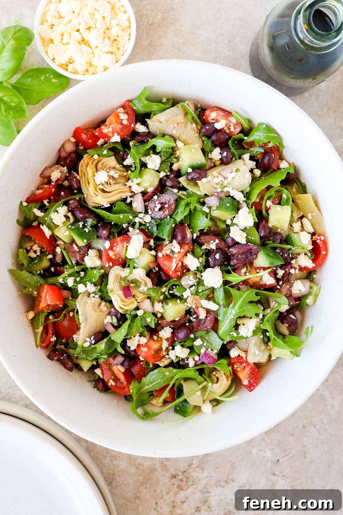 Black bean salad in a bowl. Balsamic jug, basil, feta and bowls on the side.