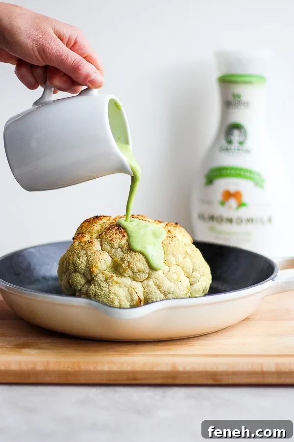 Avocado sauce being poured over a roasted head of cauliflower.