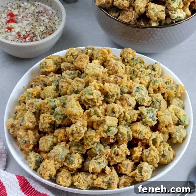 breaded fried okra in a white bowl with spicy vinegar dipping sauce on the side