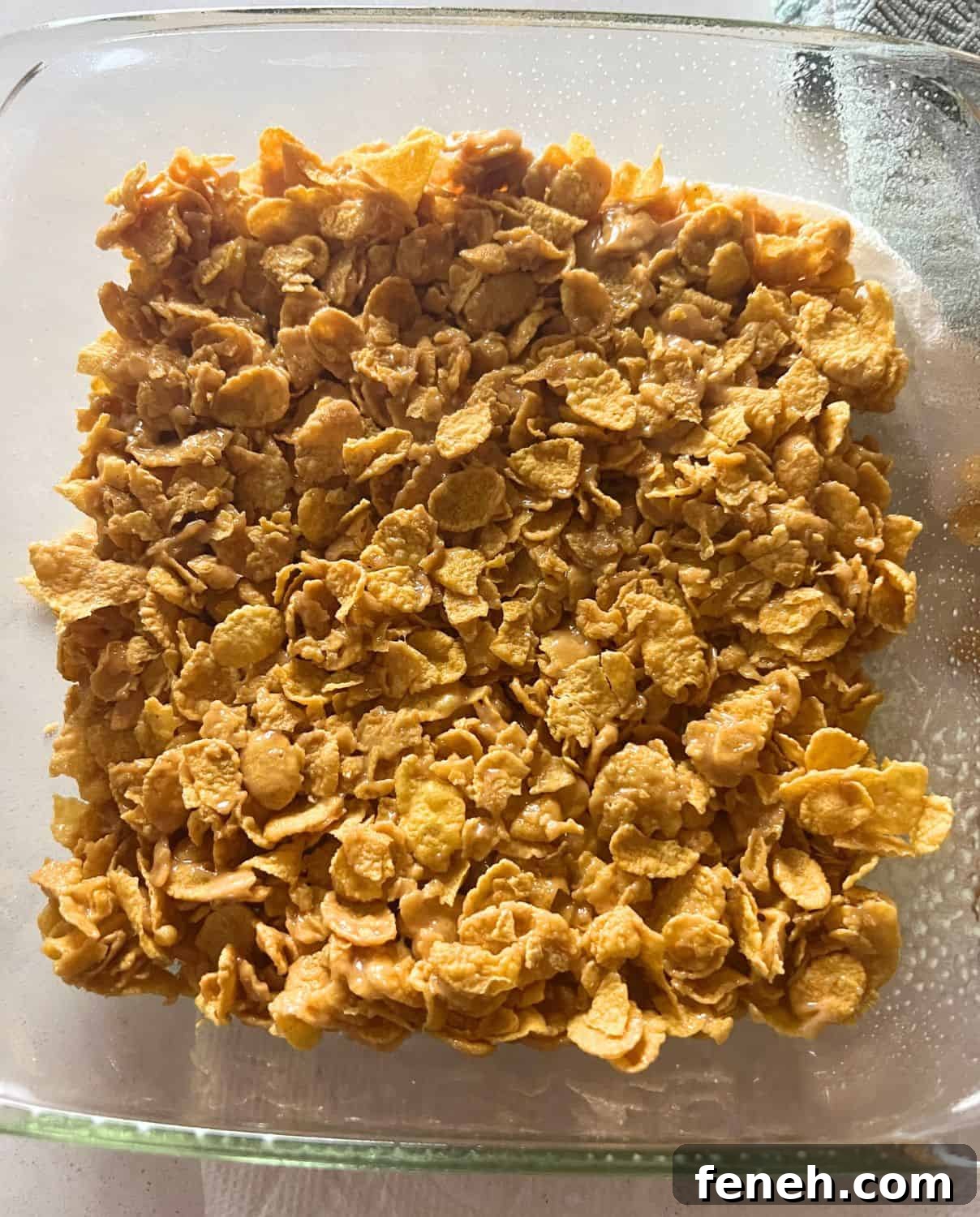 Cornflake peanut butter bars pressed into clear pan.