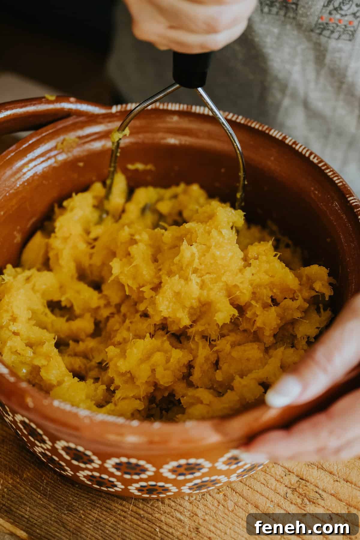 Cooked pumpkin mashed in a clay bowl with a potato masher.
