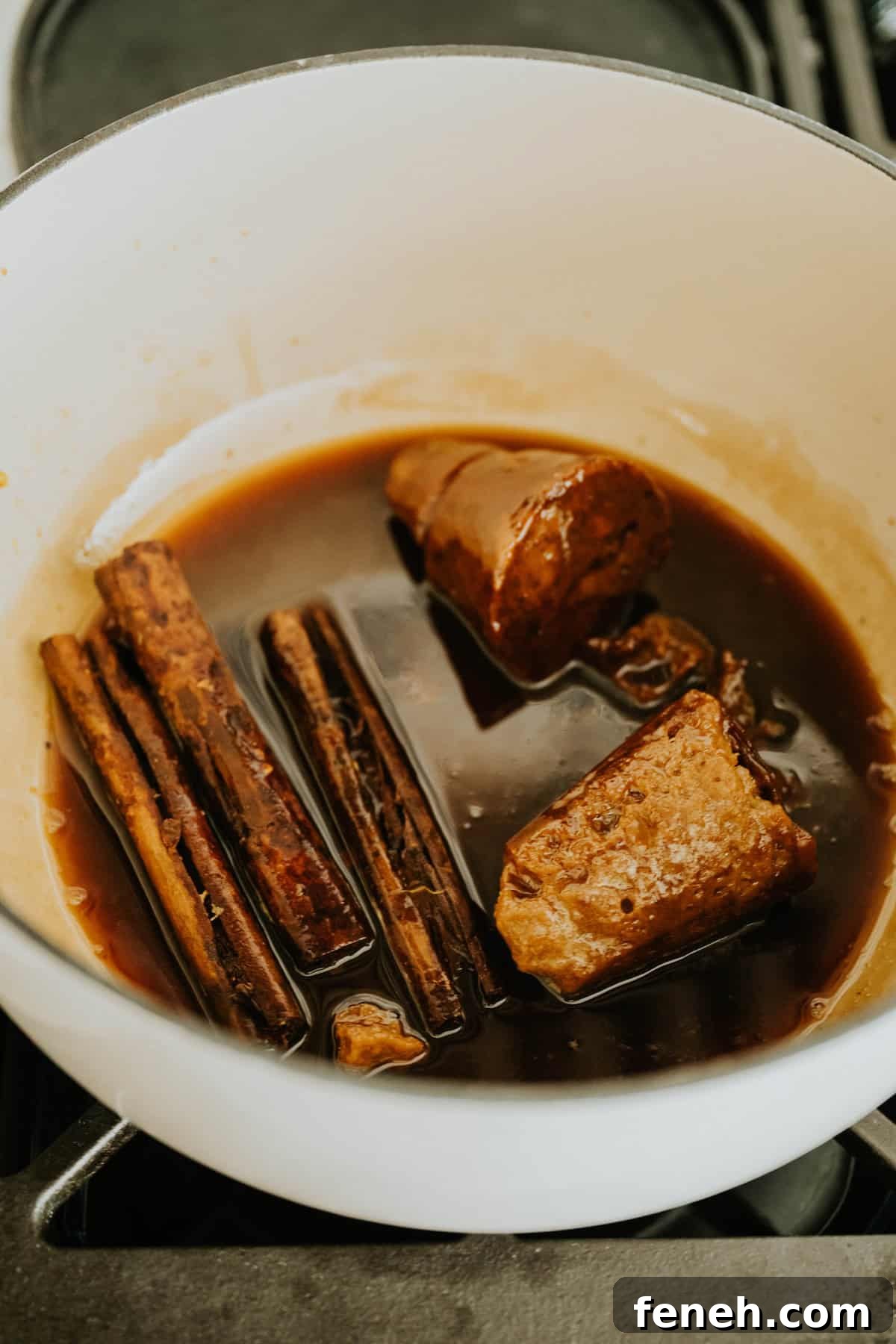 Cinnamon sticks and piloncillo simmering in syrup inside a pot.