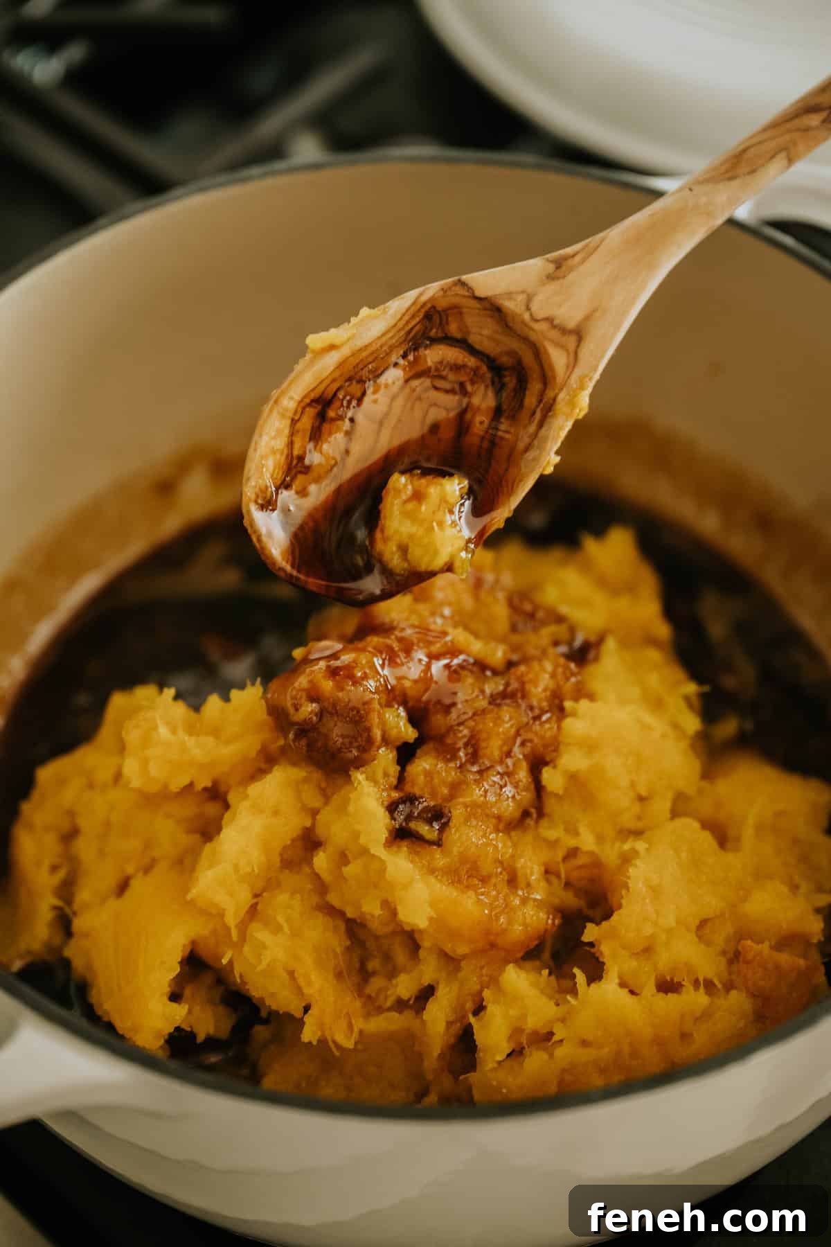 Cooked pumpkin mashed in a clay bowl with a wooden spoon.
