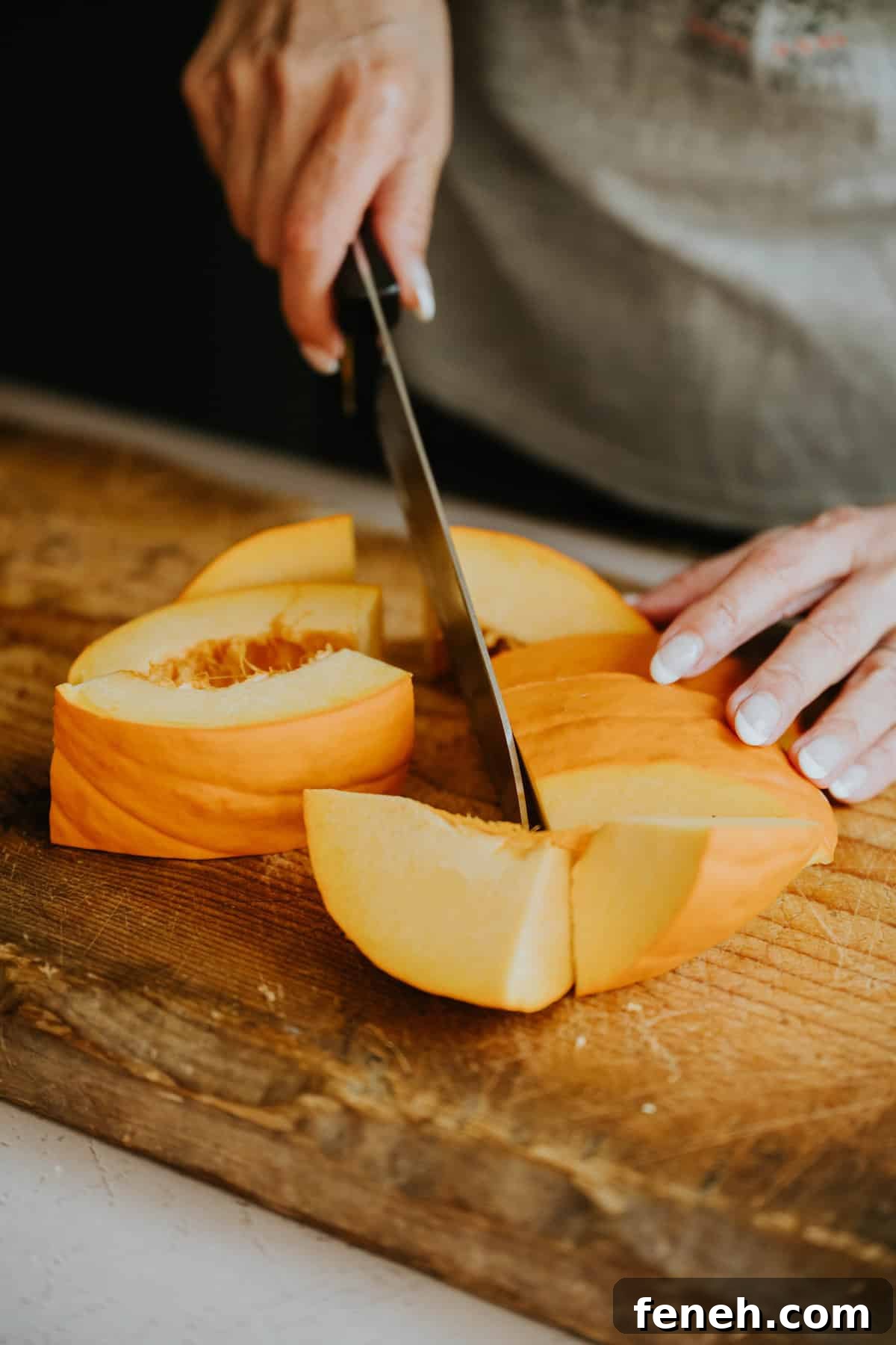 Hands slicing a fresh pumpkin on a wooden cutting board.
