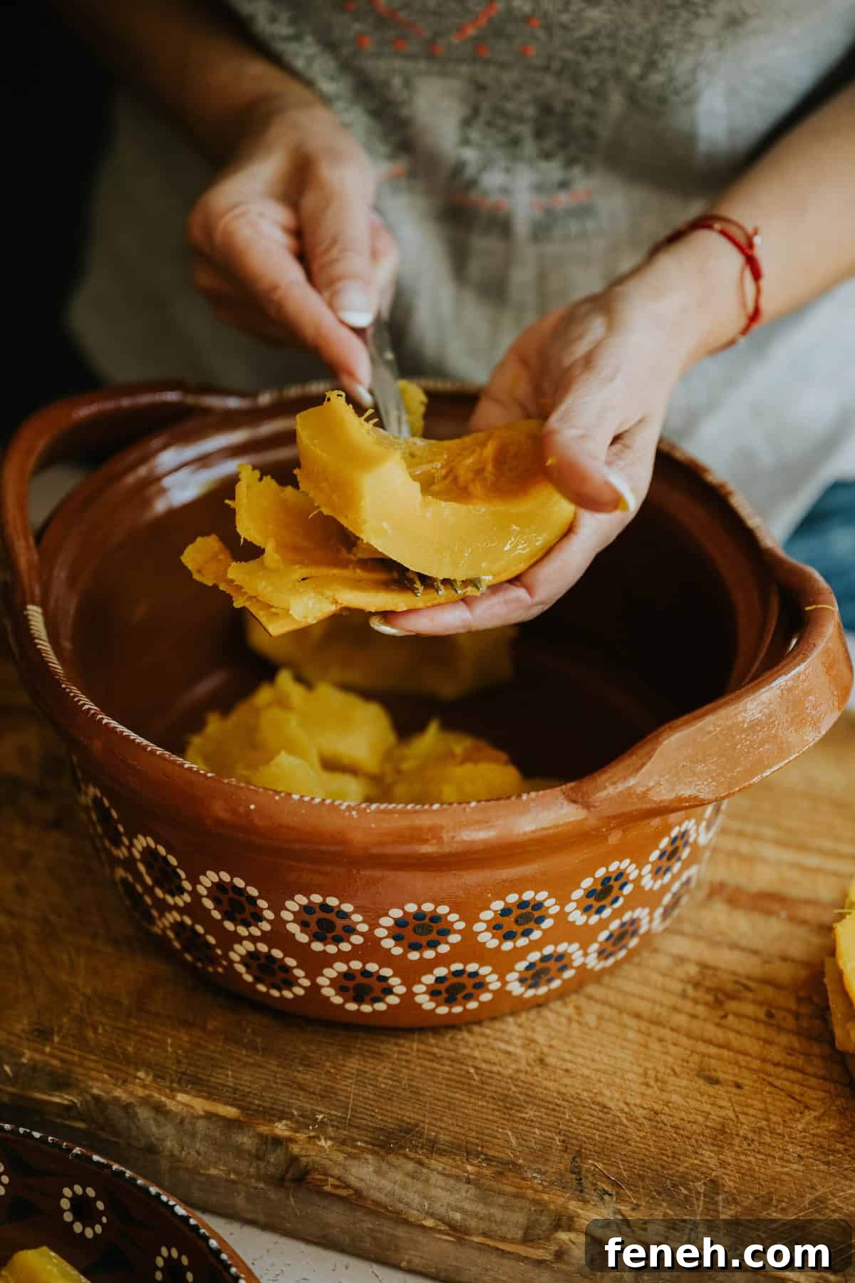 Hands peeling tender cooked pumpkin over a clay dish.