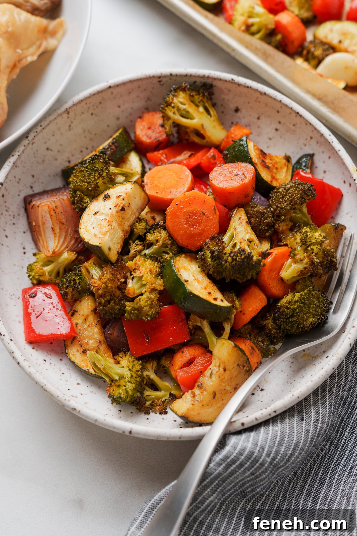 oven roasted vegetables in a bowl with a fork on a white background.