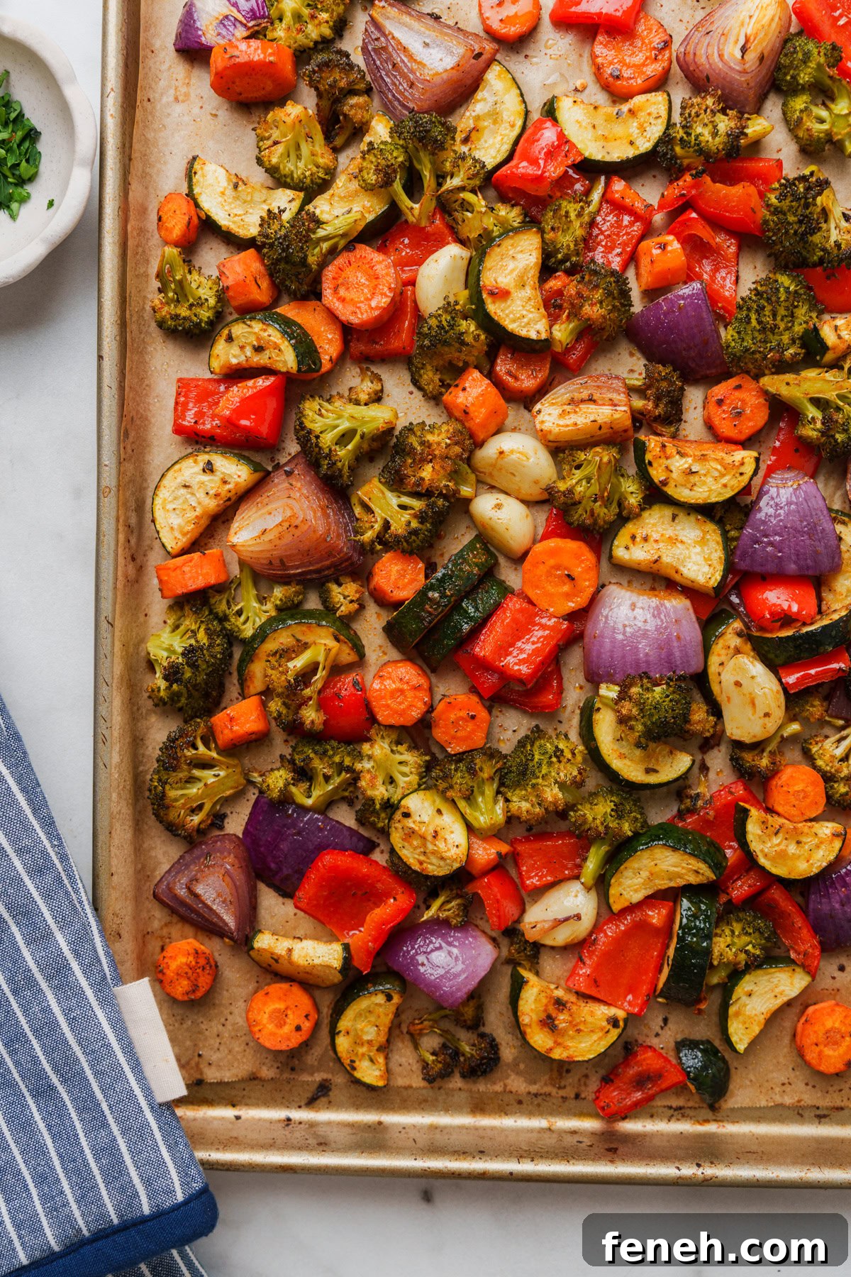 roasted vegetables in the oven in a pan with gloves on the side.