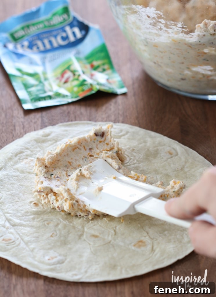 hand with spatulate spreading filling onto cheddar bacon ranch pinwheels.