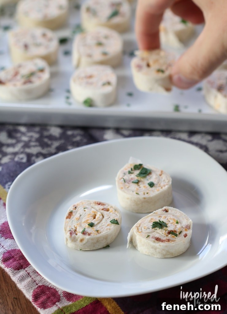 hand picking up cheddar bacon ranch pinwheels with more in the foreground.