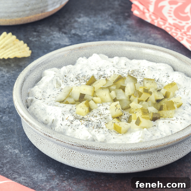 Dill pickle dip in a shallow bowl, with a second bowl of ruffled potato chips for dipping.