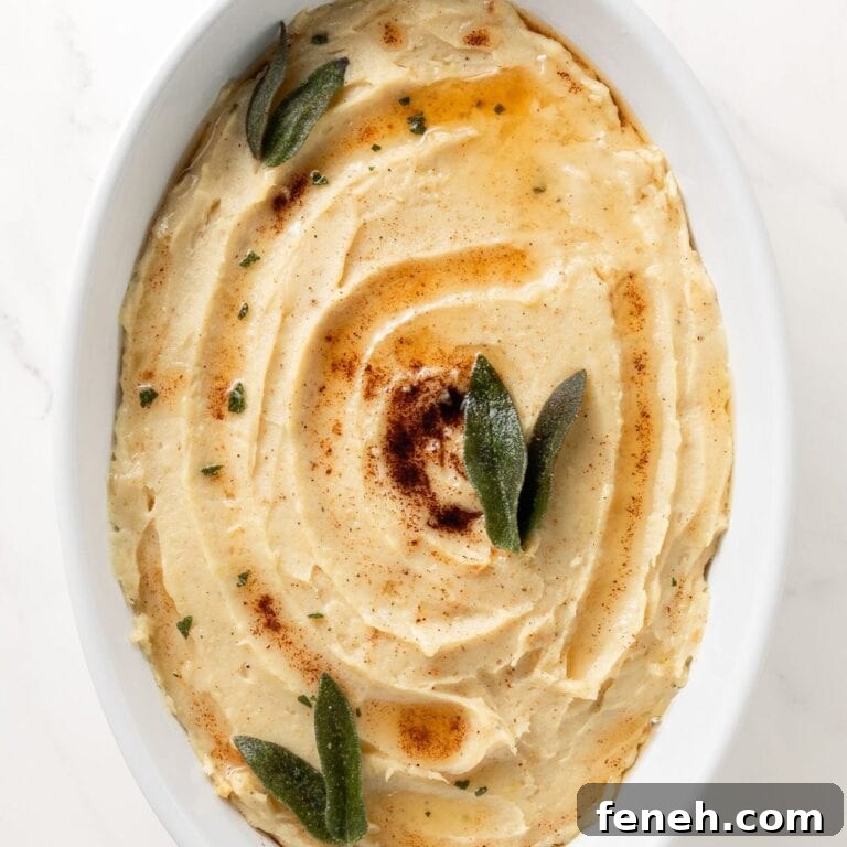 Mashed white sweet potatoes in a white oval serving dish drizzled with brown butter and garnished with sage leaves.