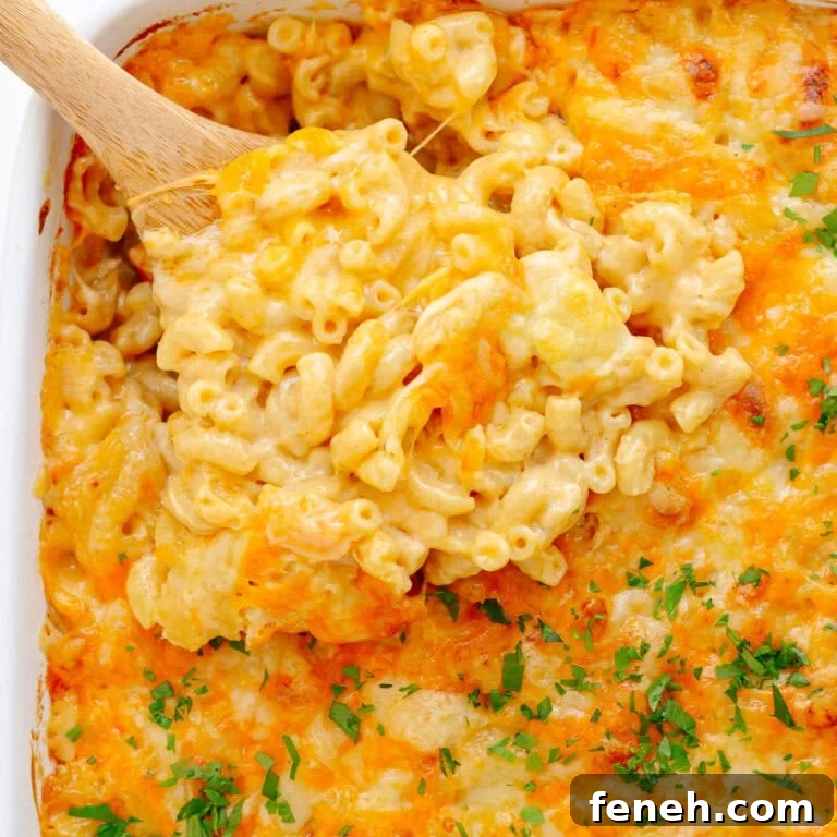 Three cheese mac and cheese being scooped out of casserole dish with wooden spoon.