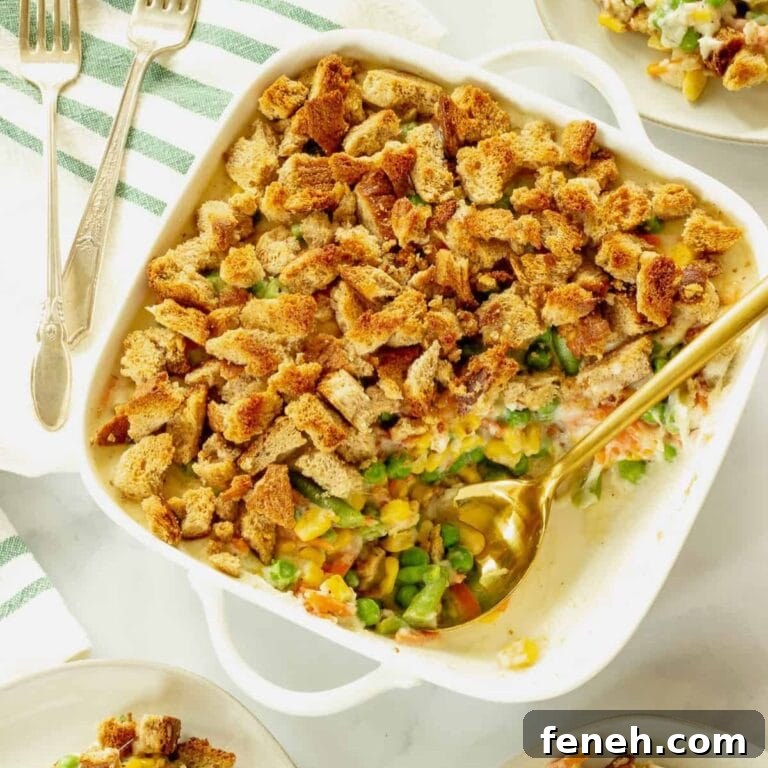 Mixed vegetable casserole in white baking dish with serving spoon scooping some out.