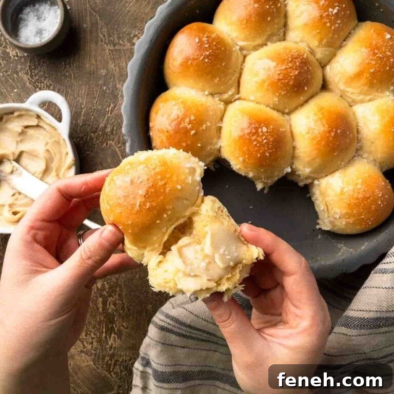 Hand holding a soft dinner roll spread with maple butter.