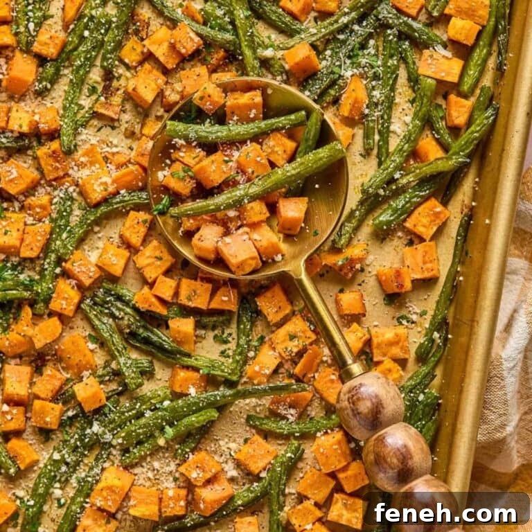Roasted sweet potatoes and green beans on a baking sheet with large serving spoon.
