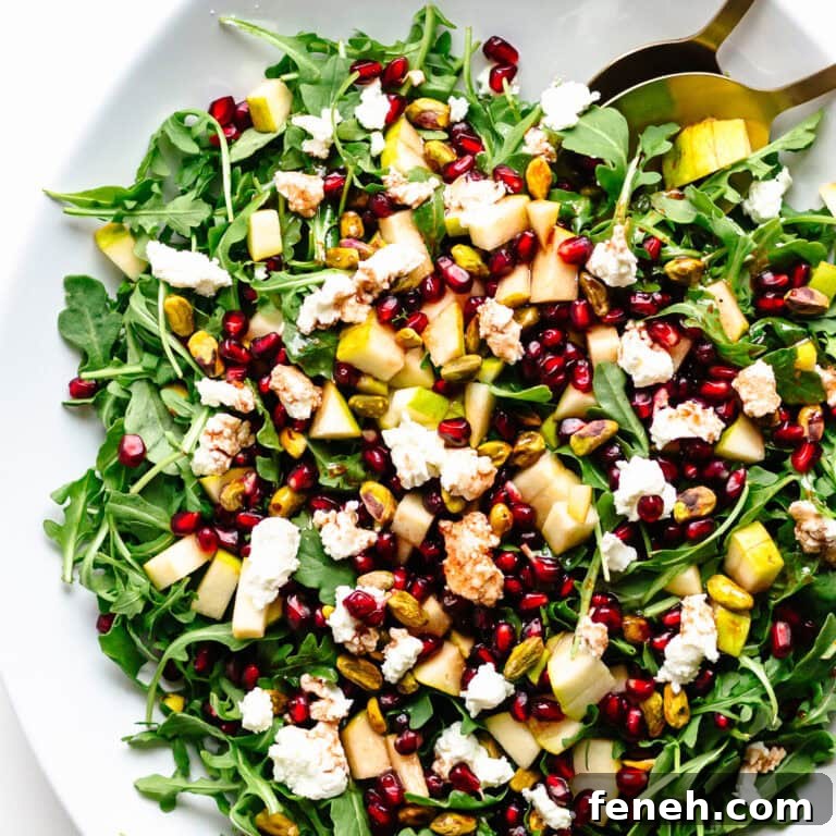 Holiday salad on a white platter with baby greens, pear, pomegranate, pistachios, goat cheese and pomegranate vinaigrette.