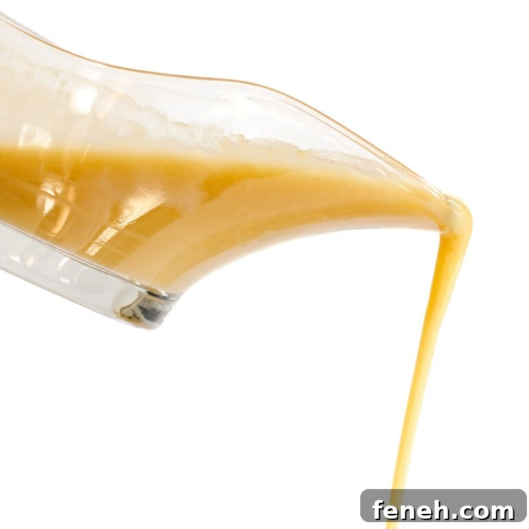 Turkey gravy pouring out of a glass gravy boat against a white background.