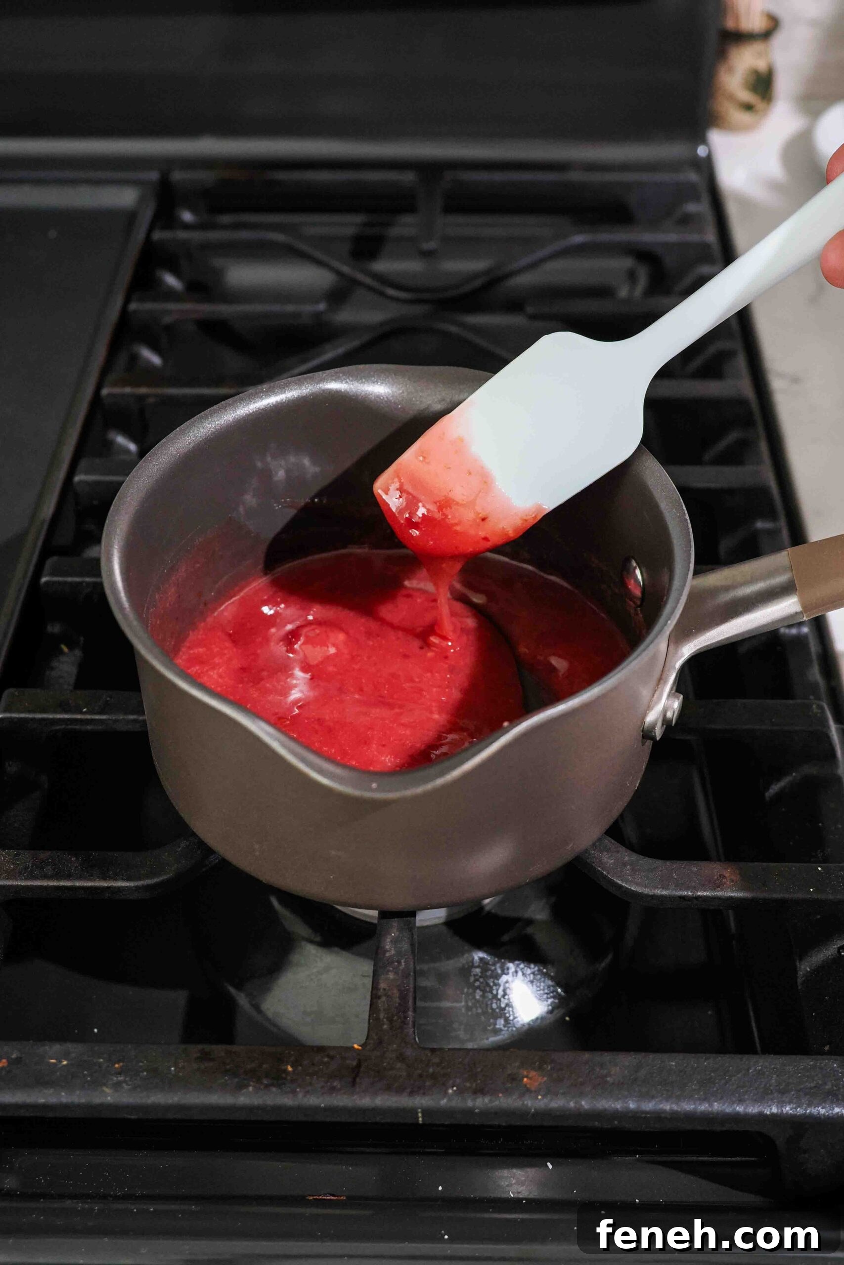 A spatula drips thickened cherry filling back into a saucepan on the stove.