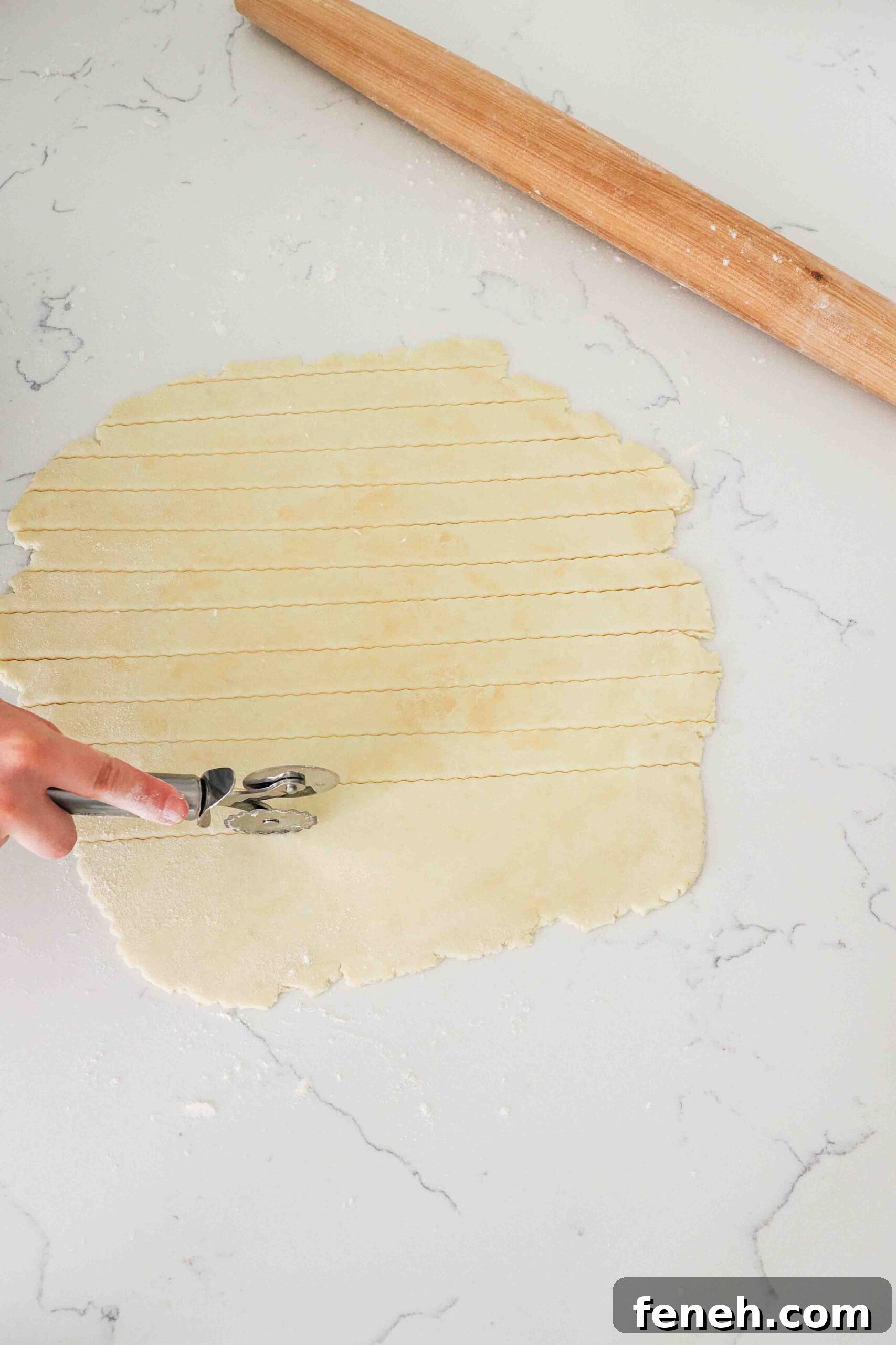 A hand uses a pastry roller to cut strips in pie dough.