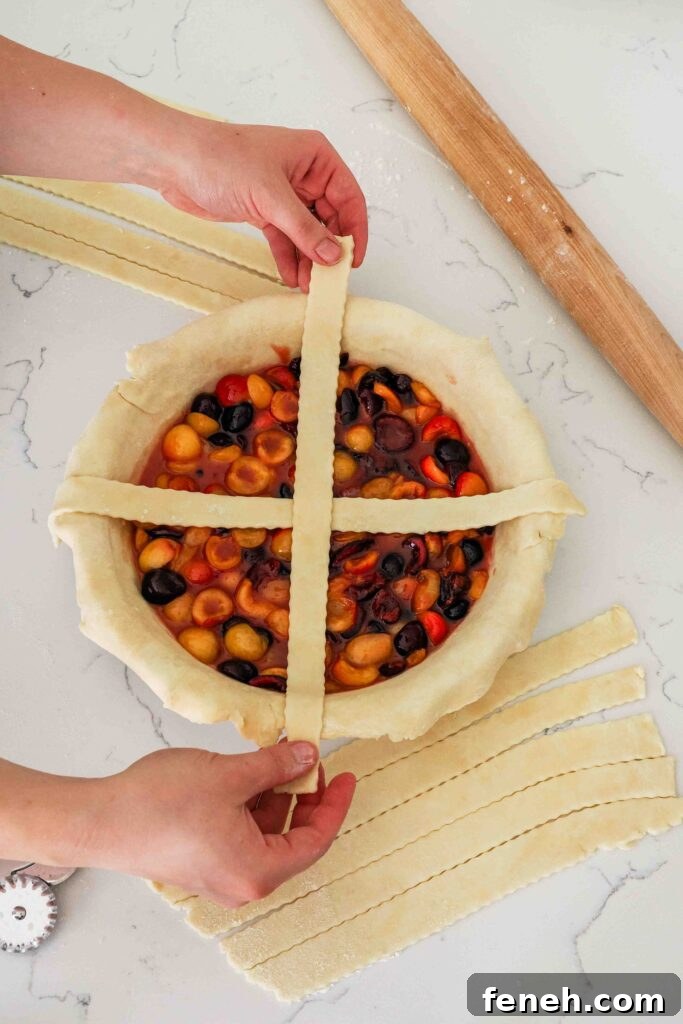 Two hands place a strip of dough over an open-faced cherry pie.