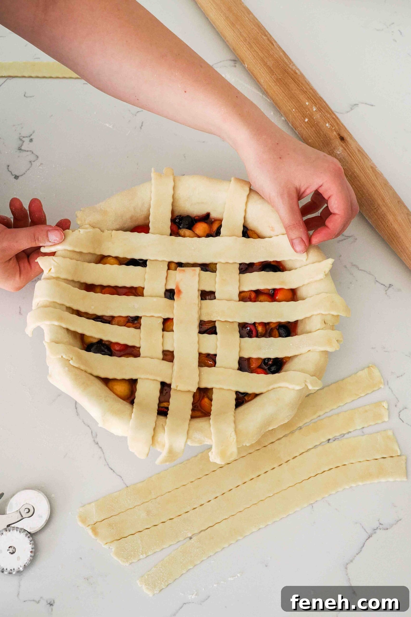 Two hands weave pie dough strips in a lattice over cherry pie filling.