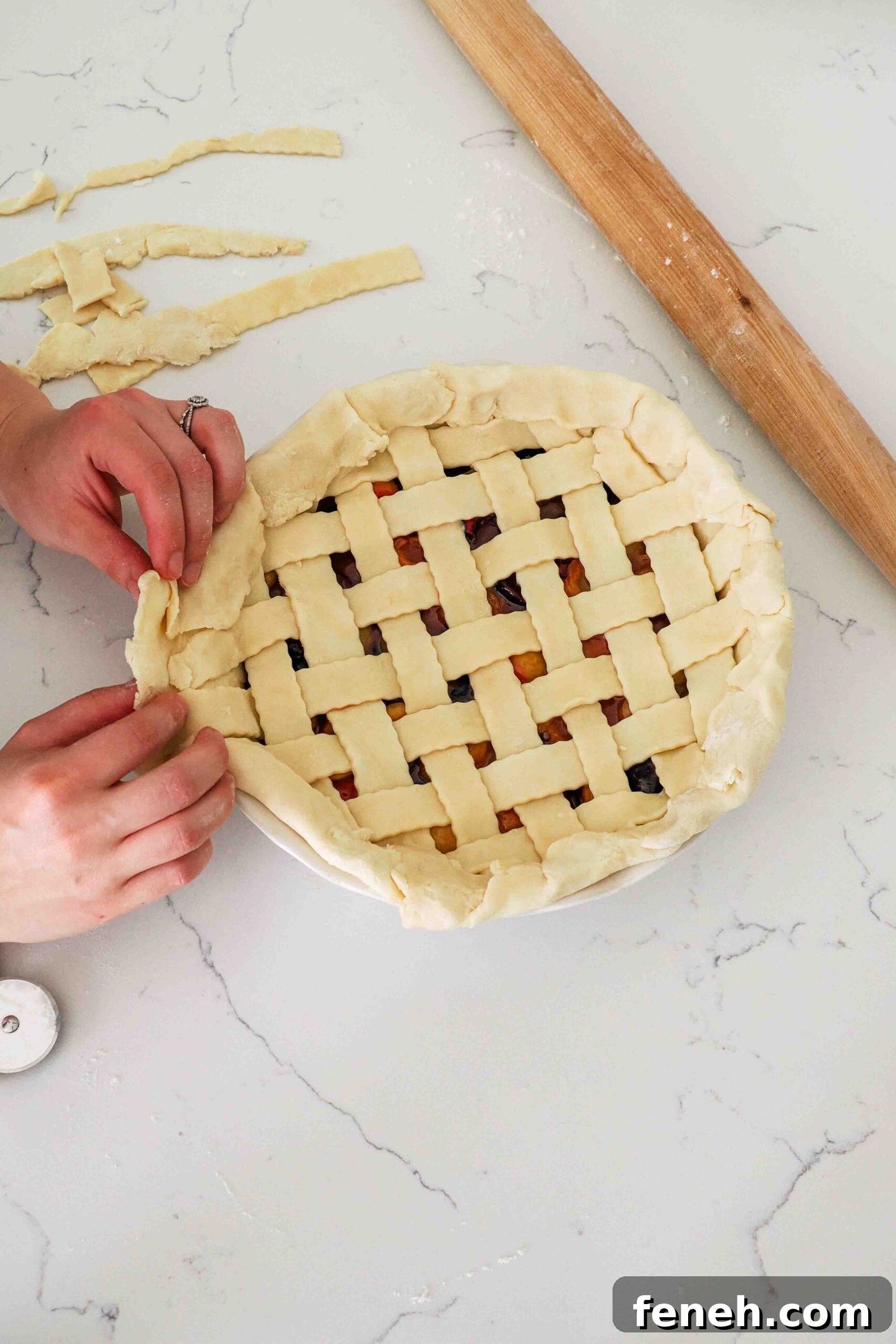 Two hands fold over the edge of a crust in a pie pan.