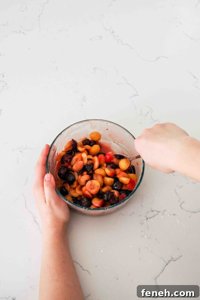 A hand stirs the cherry pie filling ingredients in a glass bowl.