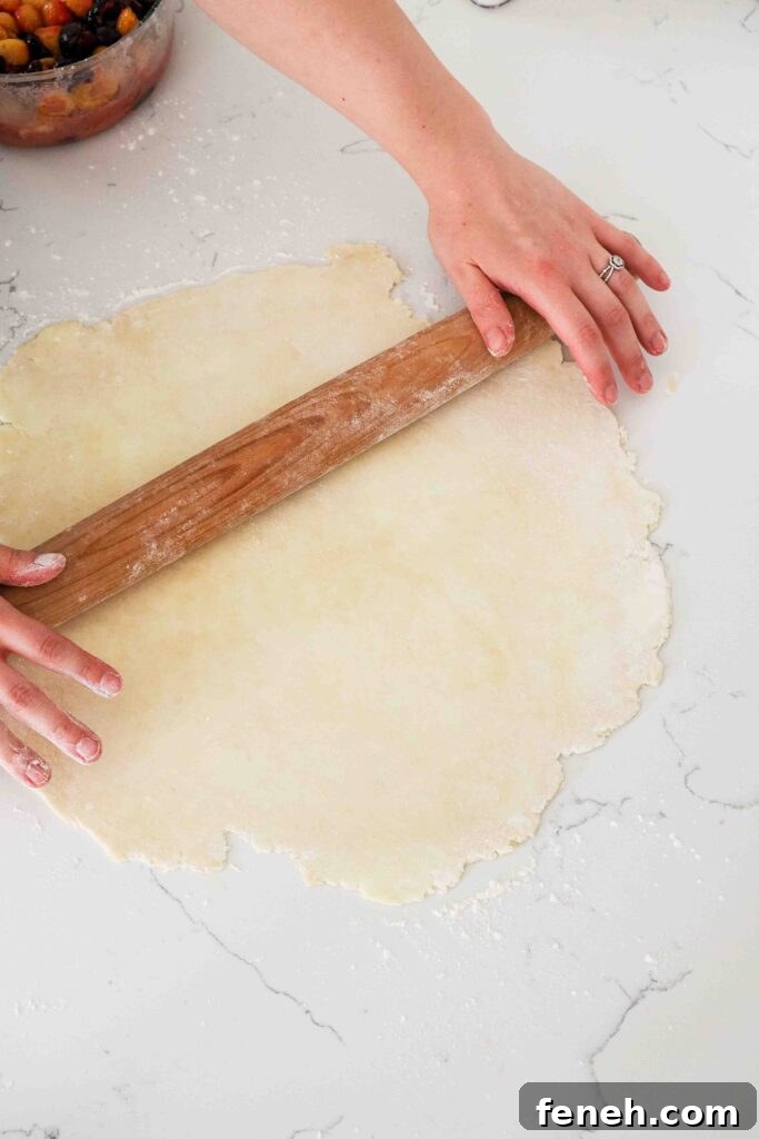 Two hands roll out a sheet of pie dough.