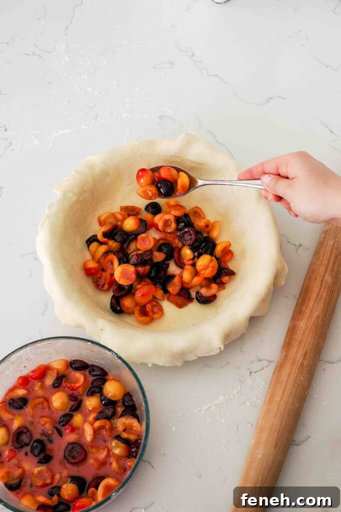 A hand spoons cherries into pie crust in a pie pan.