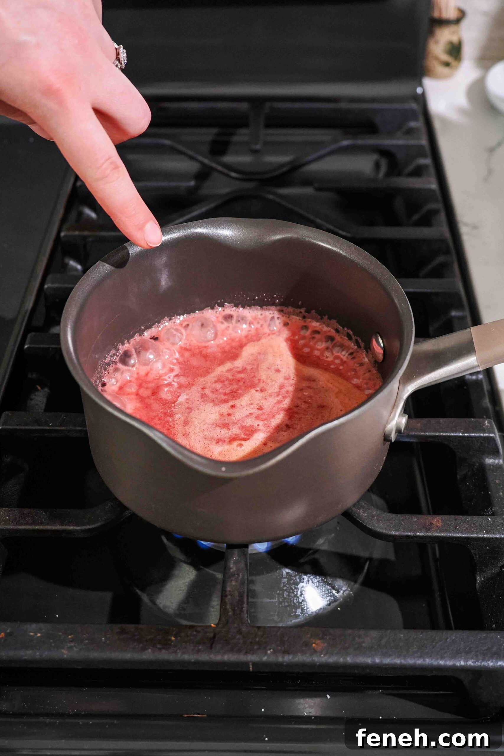 Red cherry liquid boils in a small saucepan over the stove.