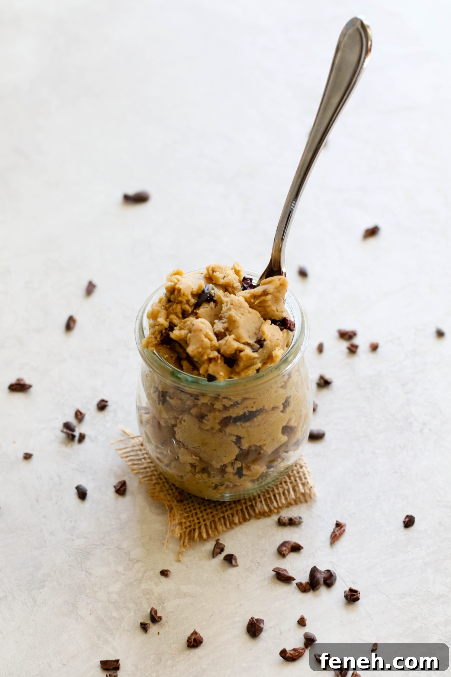 Cacao Chickpea Cookie Dough in mason jar with spoon and cacao nibs scattered