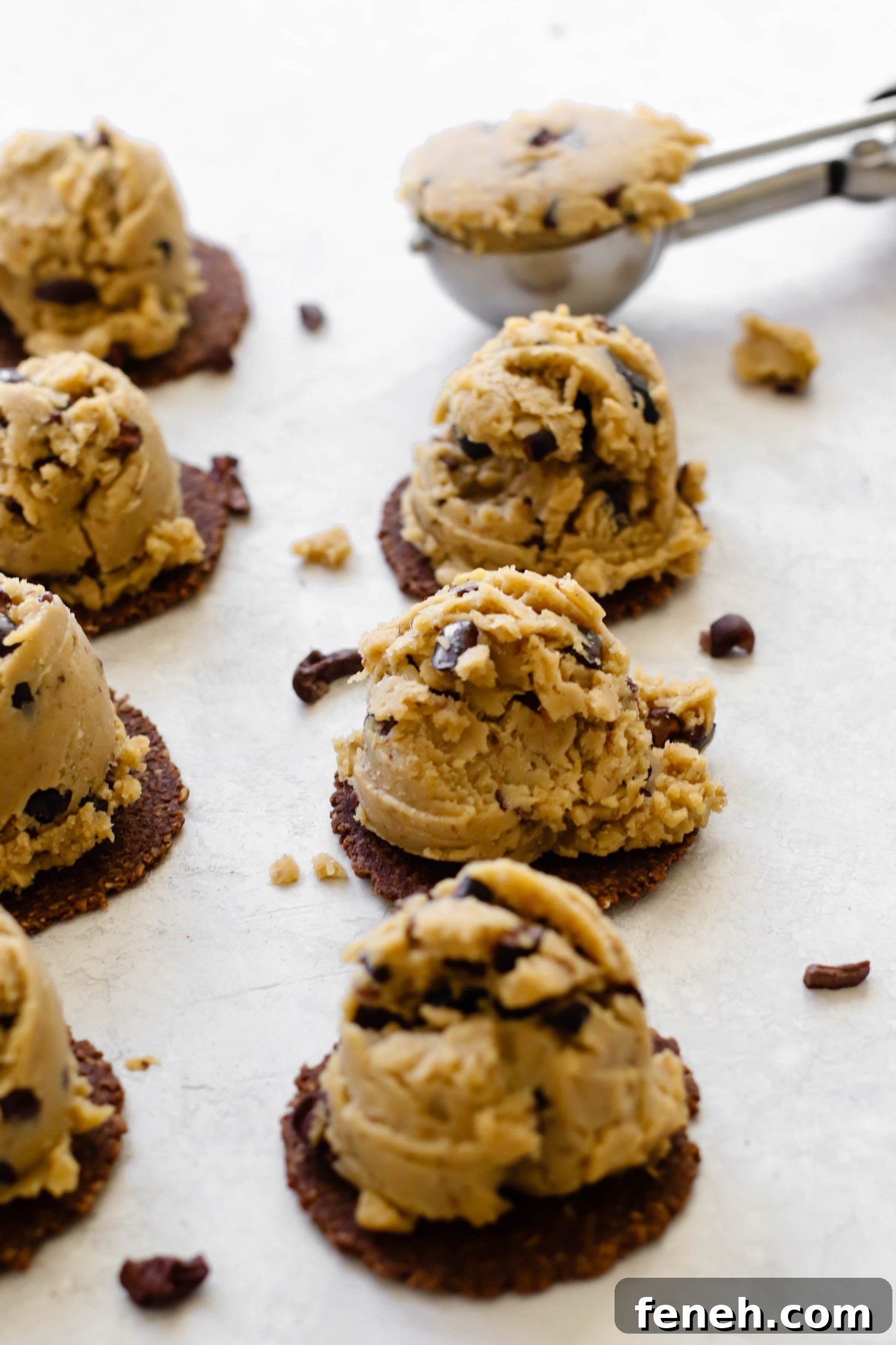Cacao Chickpea Cookie Dough scooped onto cookies with cookie scoop in background
