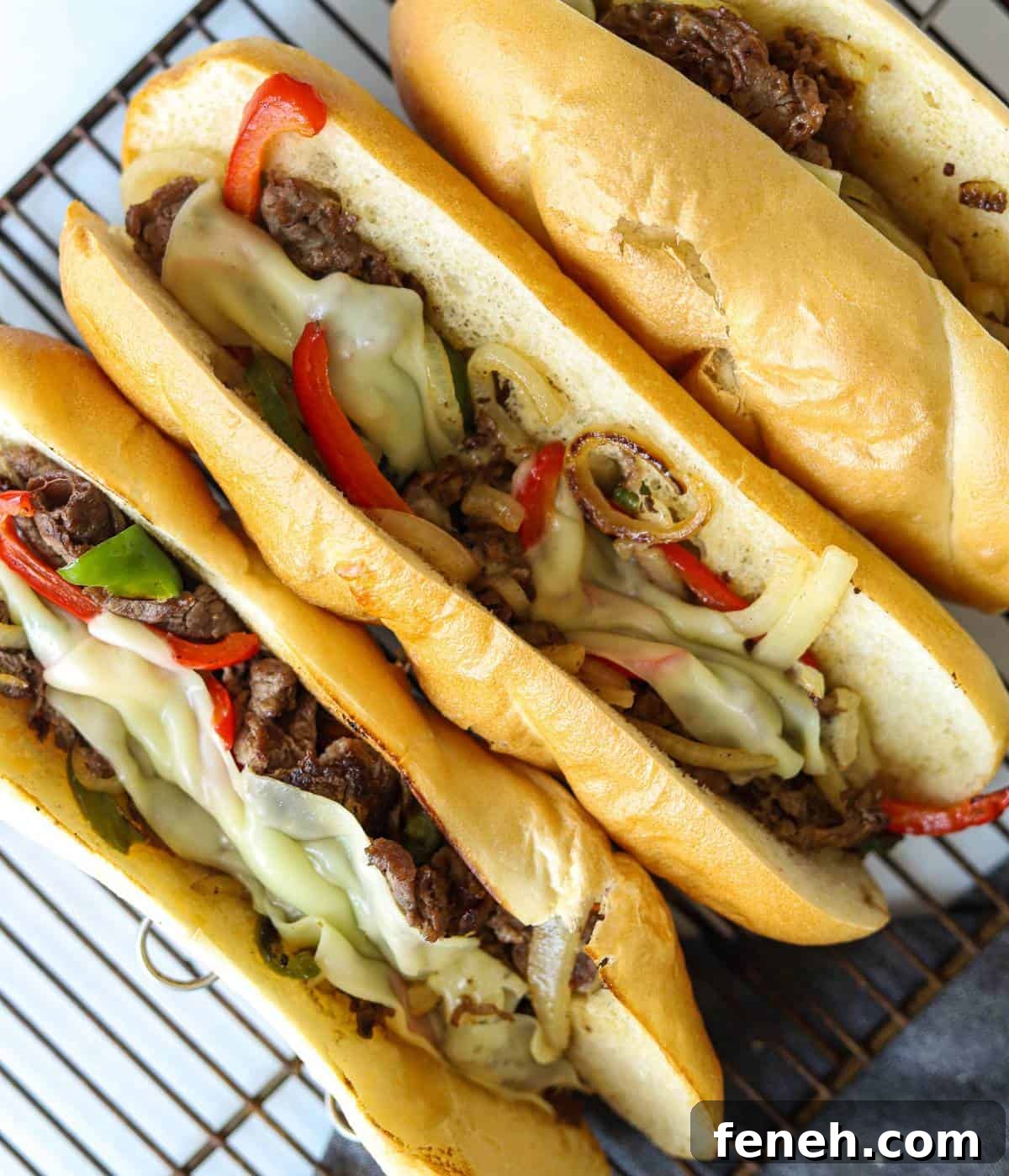 Three cheesesteaks on baking rack.