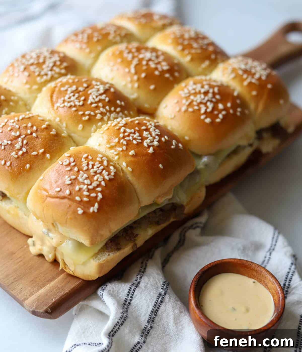 Cheeseburger sliders on wooden platter with side of sauce.