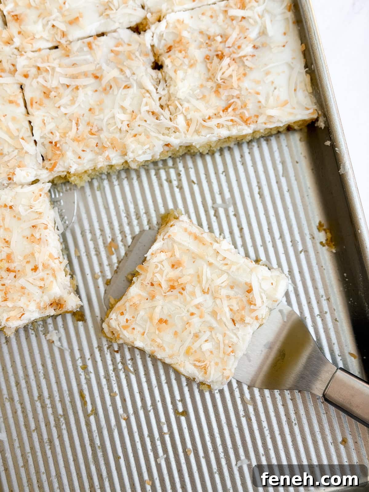 a few slices of coconut texas sheet cake on a cookie sheet after cutting.