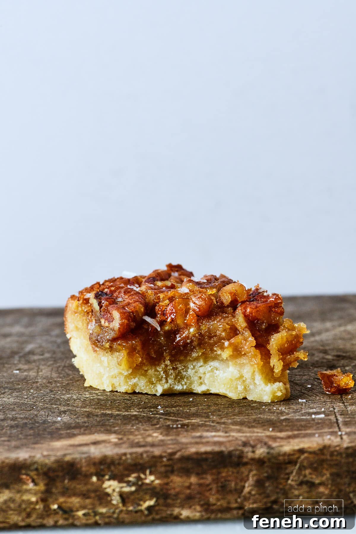 Pecan pie bar on a wooden board with a bite out of it.
