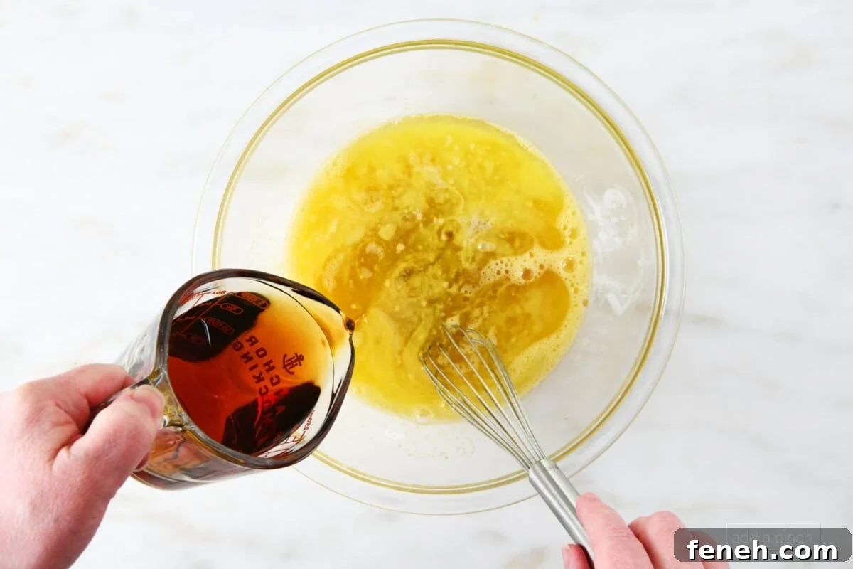 Adding maple syrup to sugar and egg mixture in a glass bowl.